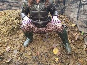 Princess in down jacket, latex pants and rubber boots fisting on dung heap