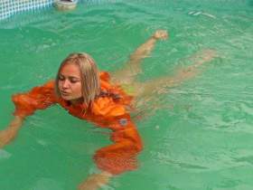 Christina in an orange down jacket swims in the pool